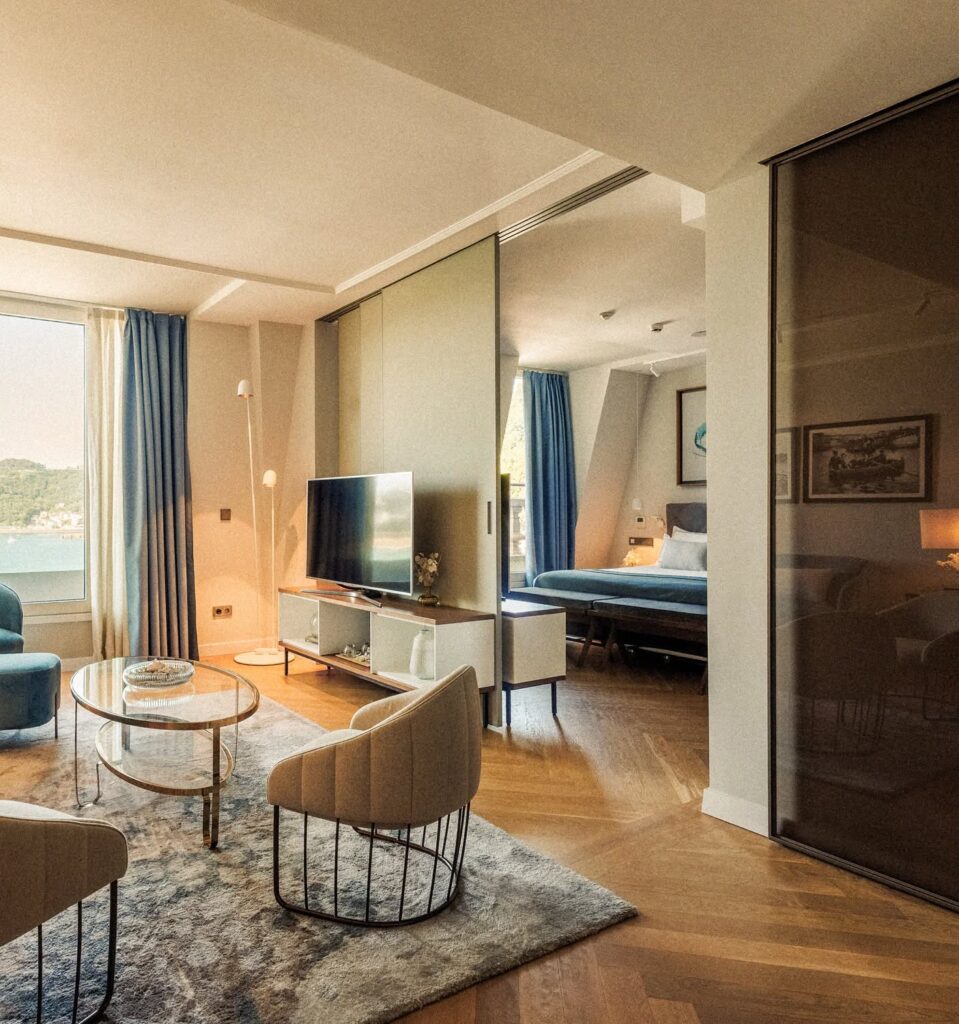 Suíte de luxo no Lasala Plaza Hotel San Sebastian com sala integrada, mobiliário contemporâneo e vista panorâmica para o mar através de grandes janelas.