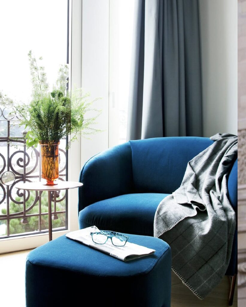 Detelhe de poltrona de veludo azul em quarto do Lasala Plaza Hotel San Sebastian, evidenciando texturas ricas e luz natural da sacada.