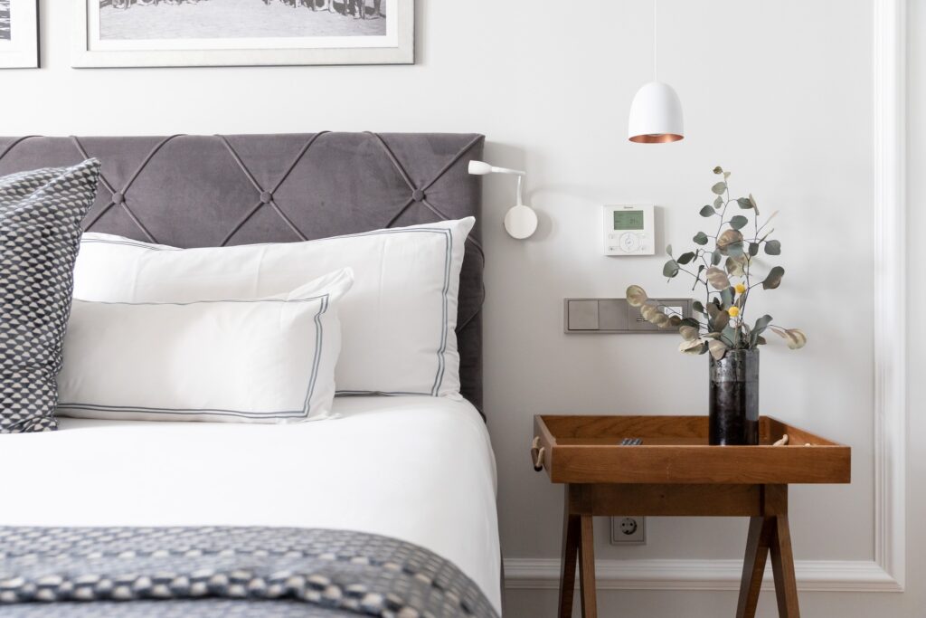 Detalhe de dormitório no Lasala Plaza Hotel San Sebastian com cabeceira em veludo cinza, mesa lateral de madeira e design contemporâneo.