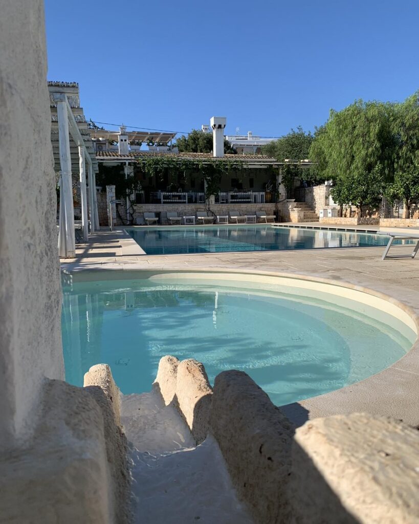 Vista vertical da piscina e jardins de hotel italiano com paisagem ensolarada e arquitetura mediterrânea.