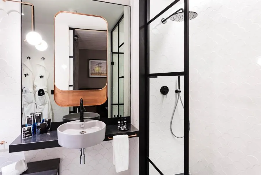 Detalle de banheiro com revestimento em escama, espelho de cobre e box industrial no One Shot Tabakalera House San Sebastian.