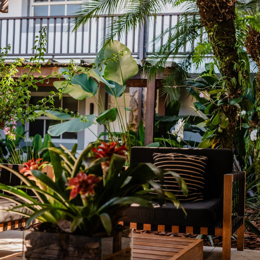 Poltrona de design em madeira e jardim tropical com bromélias vermelhas na Pousada Literária.