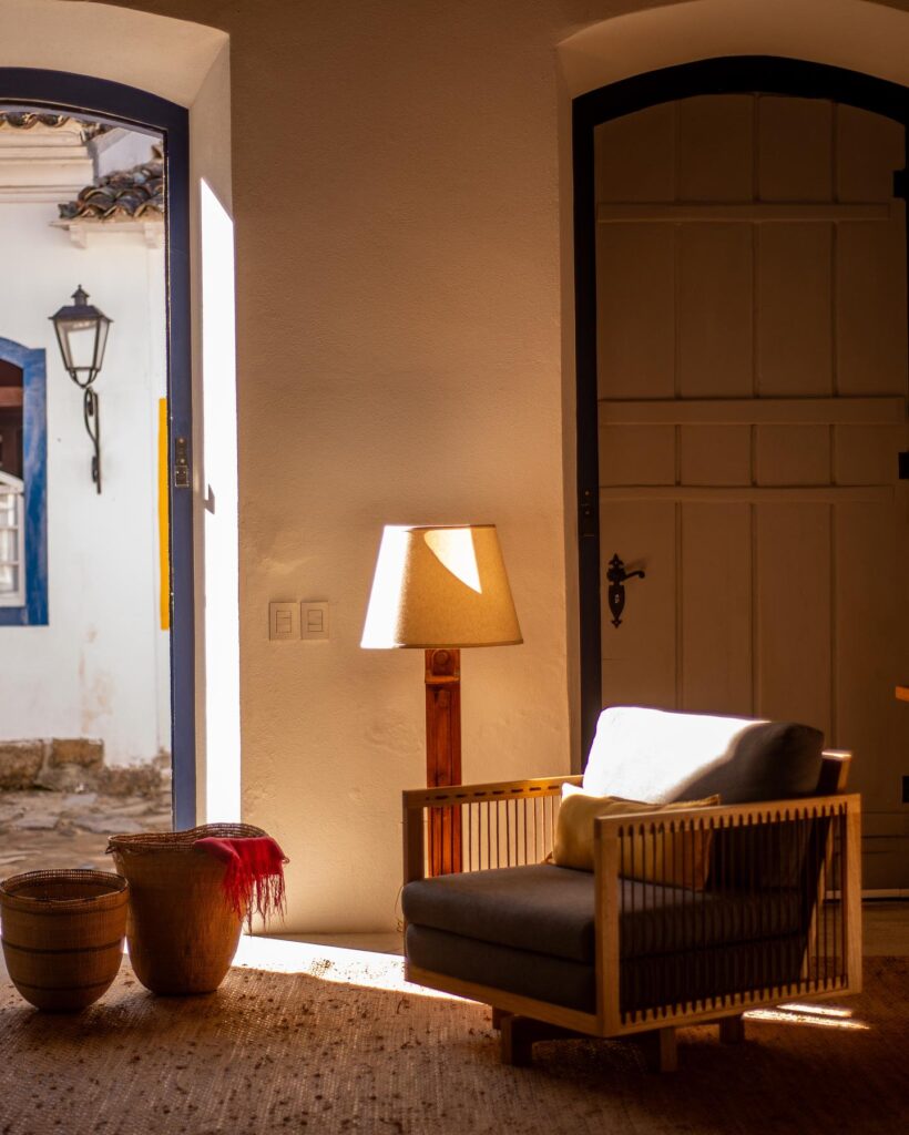Canto de leitura na Pousada Literária com poltrona de design, cestos de palha e iluminação acolhedora.