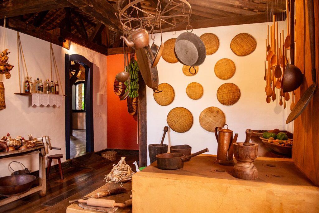 Cozinha rústica da Pousada Literária com fogão a lenha e decoração de peneiras de palha na parede.