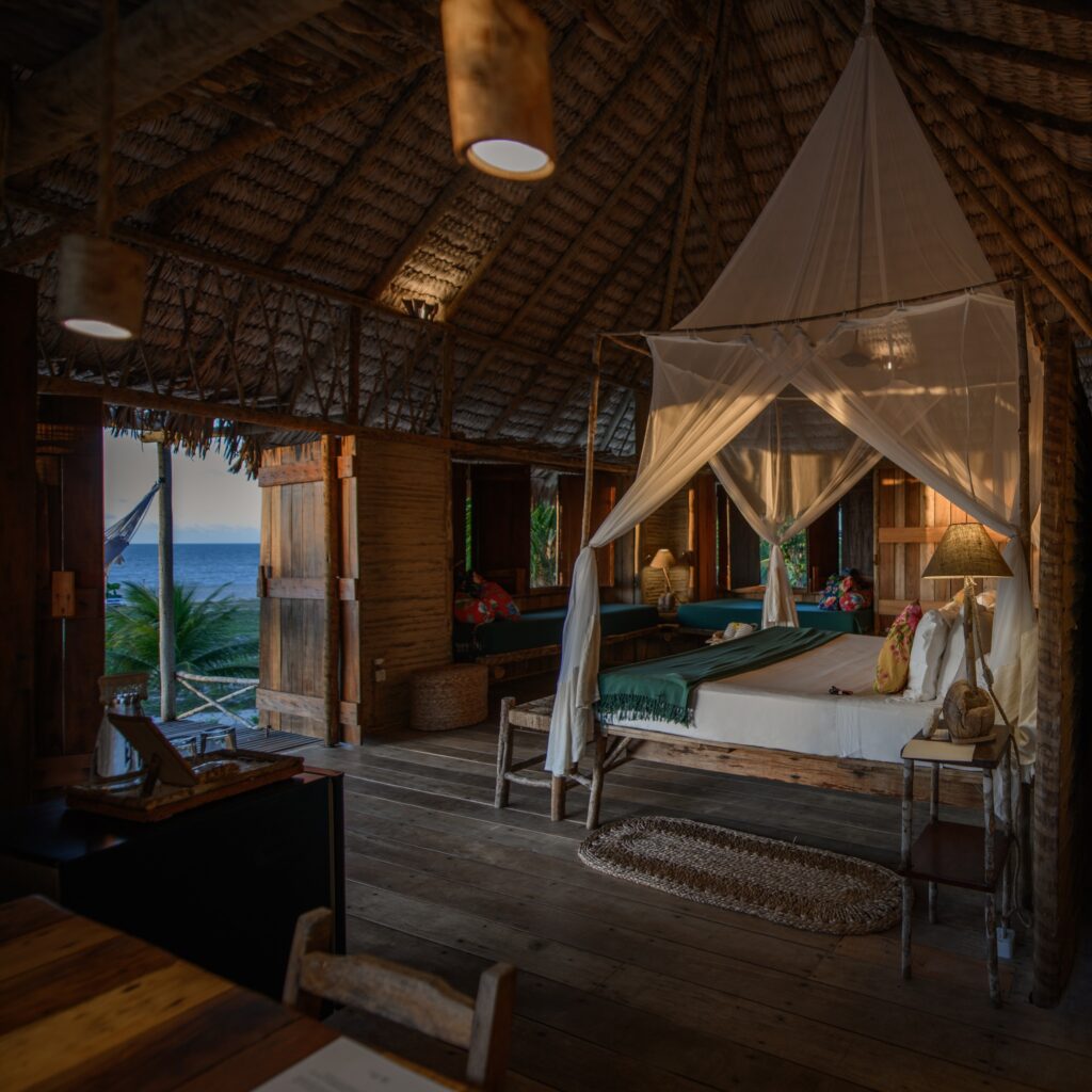 Interior aconchegante de quarto no Rancho do Peixe com dossel, móveis de madeira e vista para o mar.