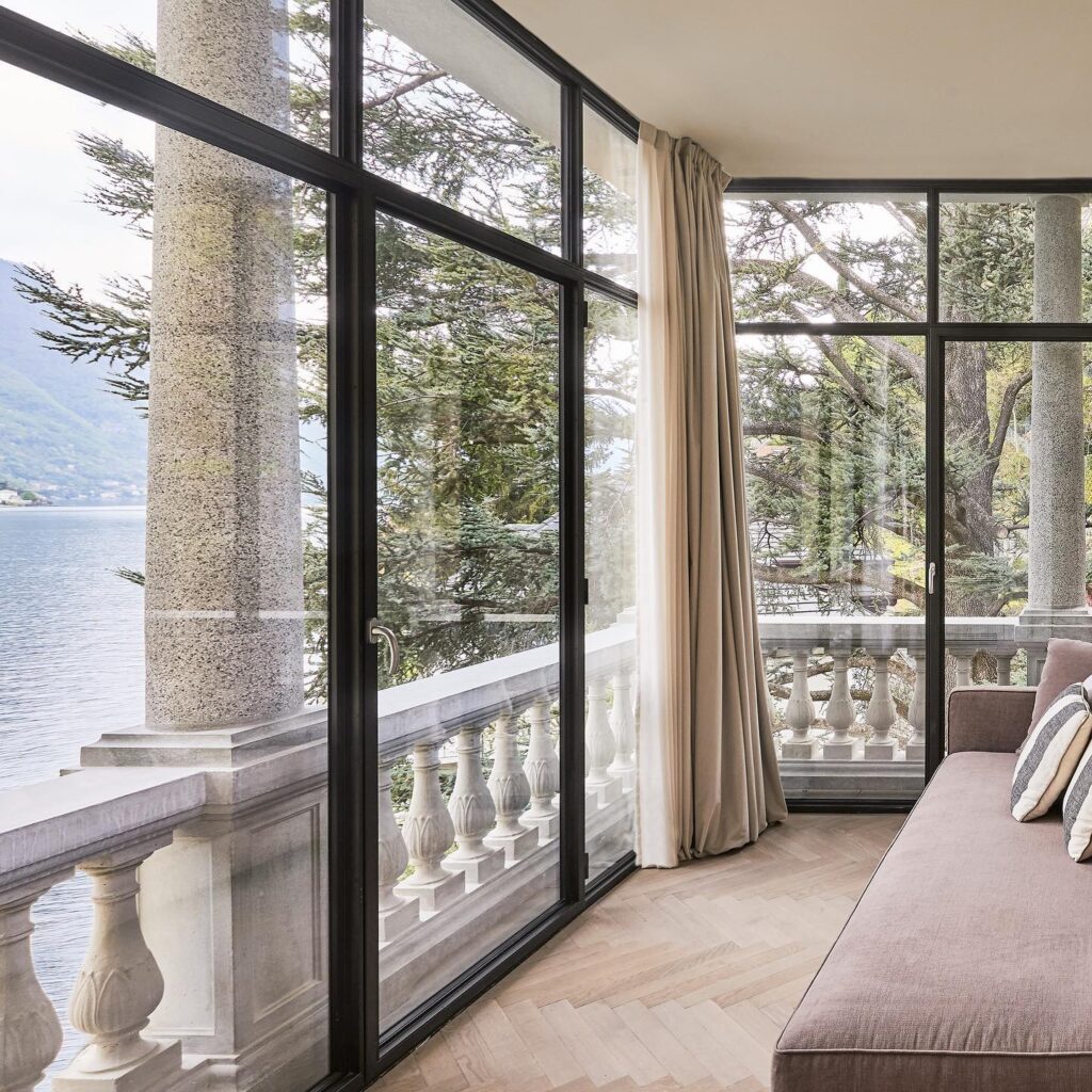 Varanda envidraçada com sofá em veludo malva e colunas de granito com vista para o Lago di Como no Villa Làrio.