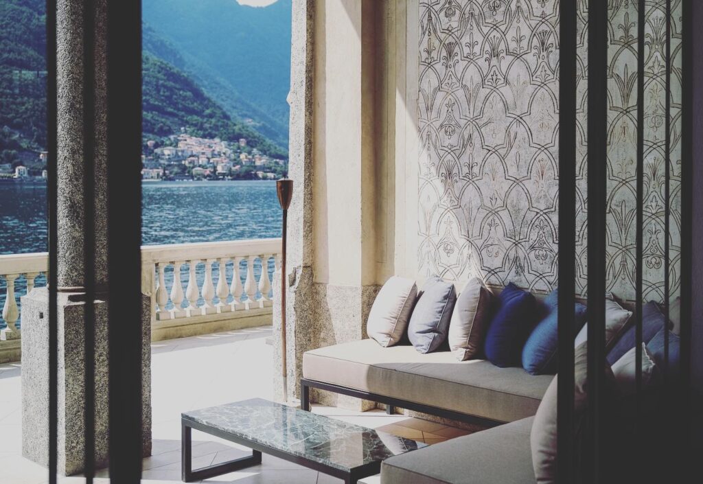 Loggia com painéis arabescos em stucco e sofá de linho com vista para o Lago di Como no Villa Làrio, hotéis no lago di Como.