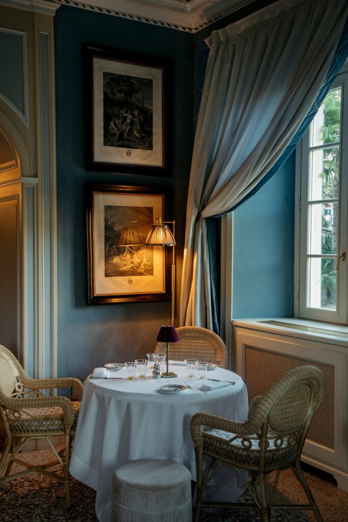 Sala de jantar com paredes teal, gravuras históricas e cortinas de seda no Passalacqua, referência de hotéis no lago di Como.