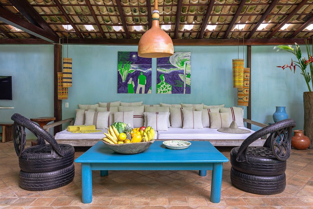 Sala de estar aberta com sofá branco, mesa azul e poltronas de pneus, ideal para relaxar em um luxuoso refúgio para páscoa.
