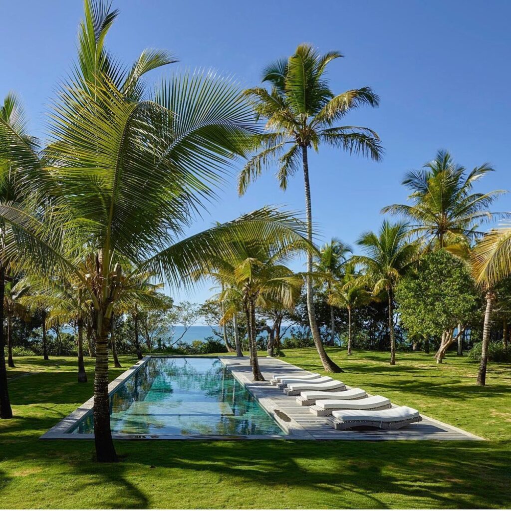 Piscina raia cercada por coqueiros com vista para o mar, o cenário dos sonhos para um refúgio para páscoa relaxante.