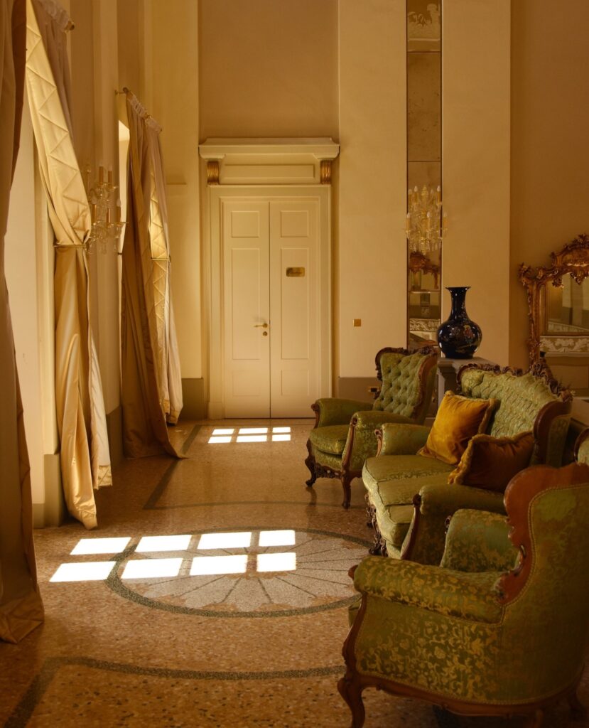 Hall de terrazzo com medalhão em mosaico e sofás em damasco verde, ambiente histórico dos hotéis no lago di Como.