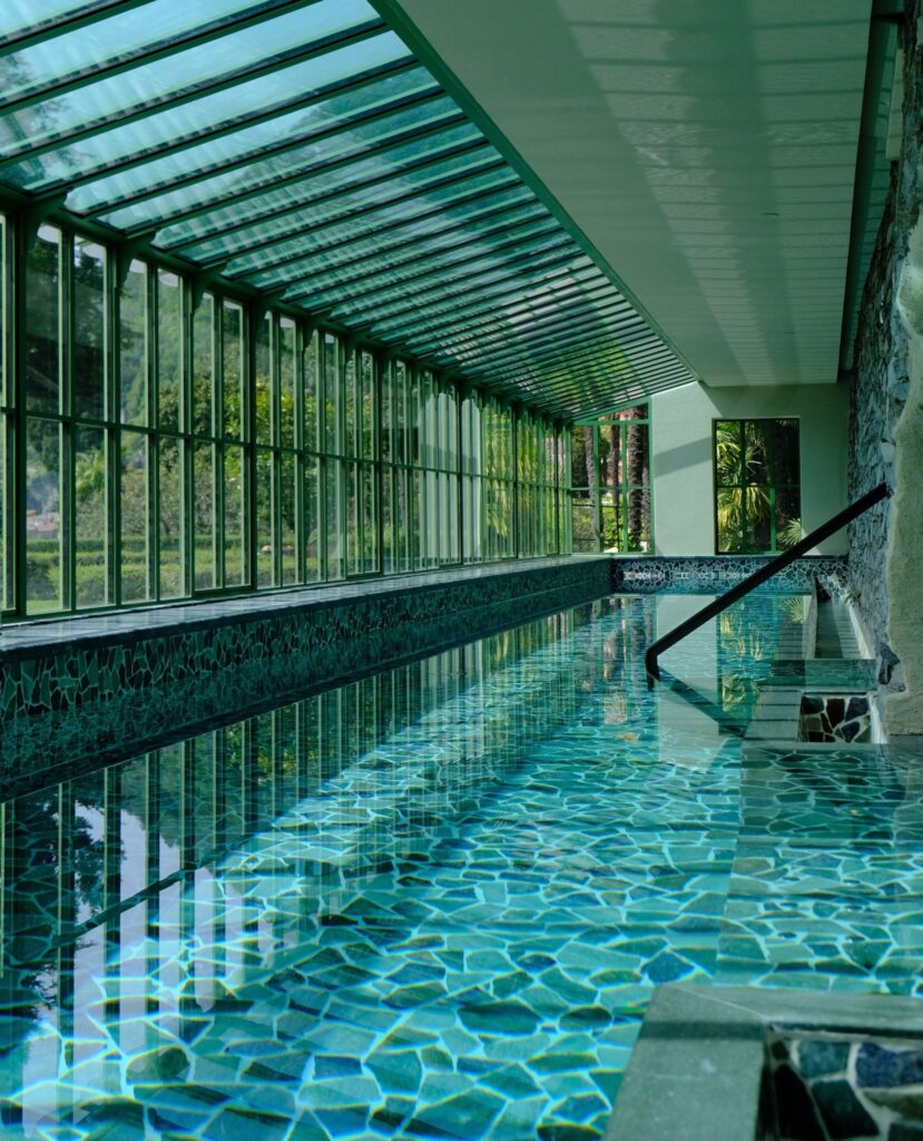 Piscina coberta de 18 metros com mosaico verde esmeralda e estrutura de vidro no spa do Passalacqua, hotéis no lago di Como.