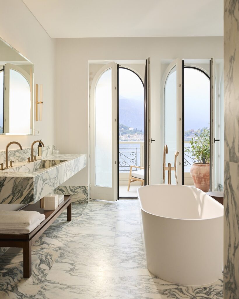 Banheiro em mármore Calacatta com banheira e portas arqueadas com vista para o lago, suíte nos hotéis no lago di Como Edition.