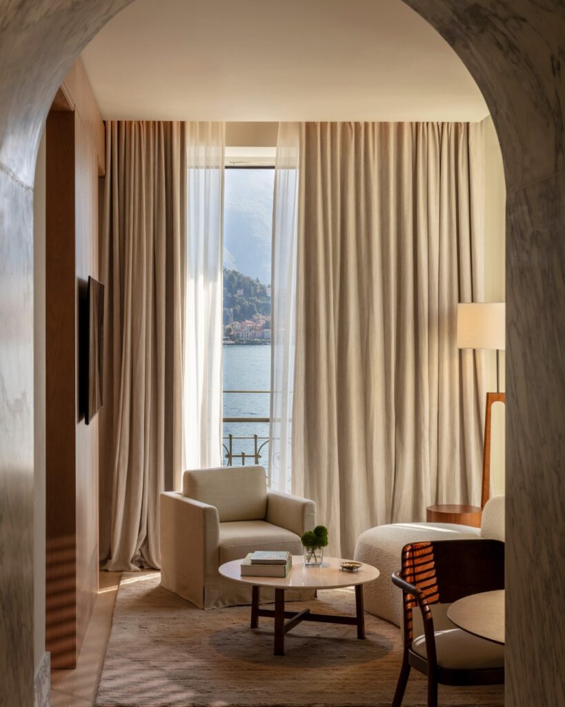 Sala de estar emoldurada por arcada histórica com sofá curvo e vista para o Lago di Como, suíte no Edition Lake Como.