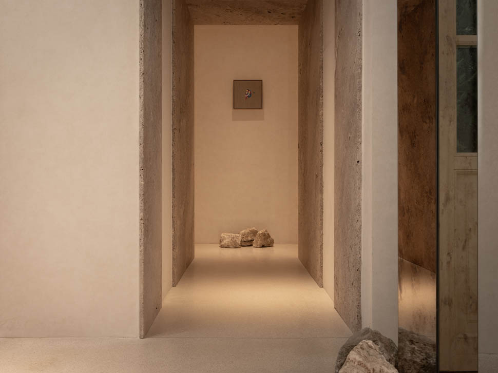 Corredor minimalista com paredes texturizadas e pedras naturais no restaurante nomos ante em Roma.