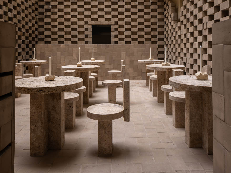 Pátio interno com mesas de pedra e paredes de tijolos geométricos no restaurante nomos ante.