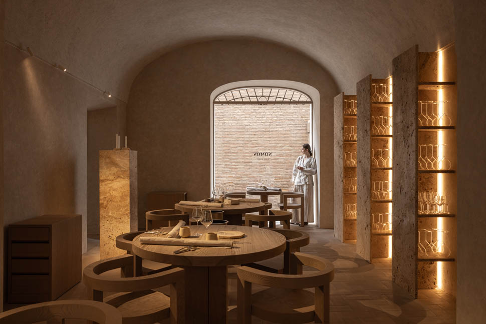 Vista interna do restaurante nomos ante destacando estantes iluminadas e mesas de madeira maciça.