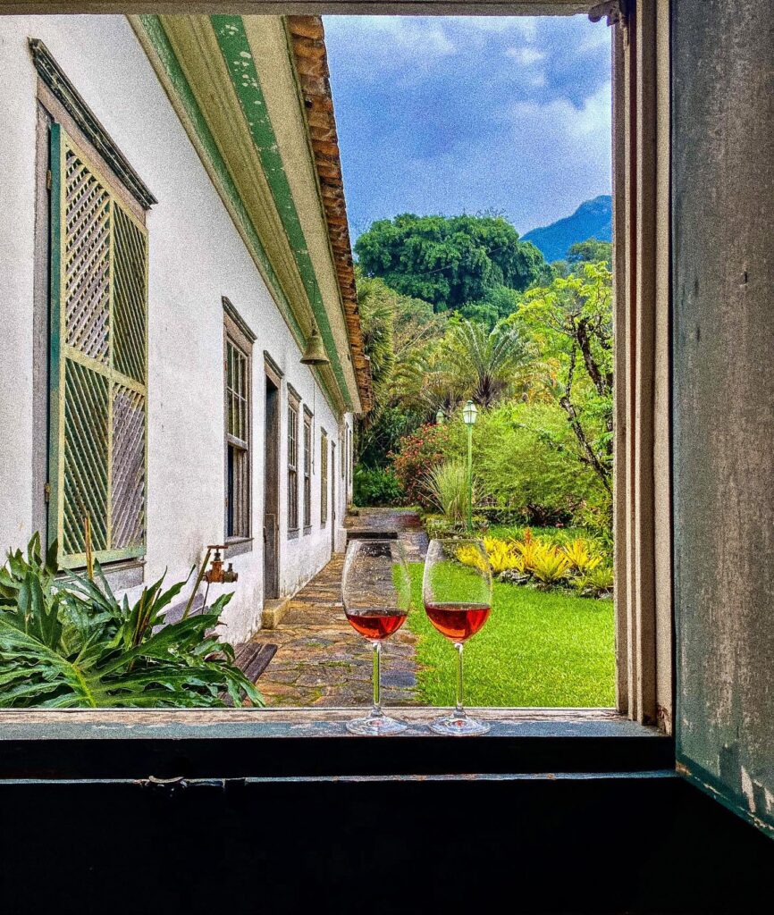Cálices de vinho em janela colonial com vista para o jardim e sino em fazendas históricas para se hospedar.