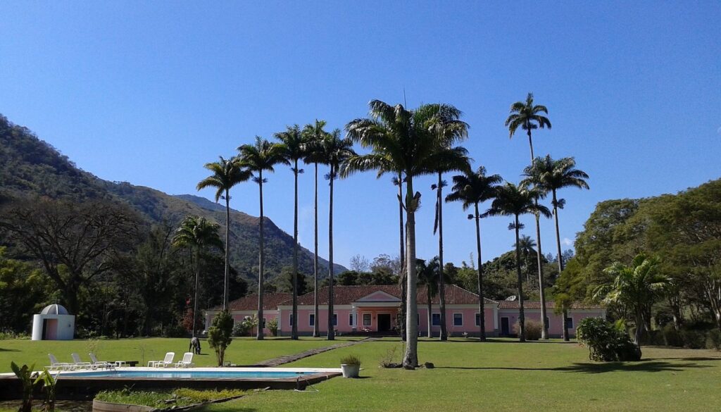 Sede neoclássica rosa com palmeiras imperiais e capela de Oscar Niemeyer em fazendas históricas para se hospedar no Rio de Janeiro.