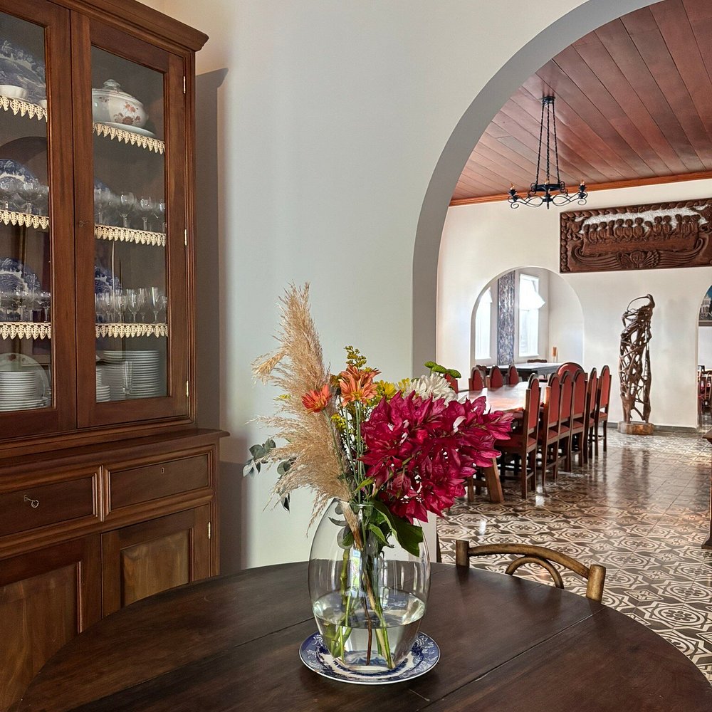 Cristaleira de madeira e arranjo de flores em sala de jantar de turismo histórico preservado.