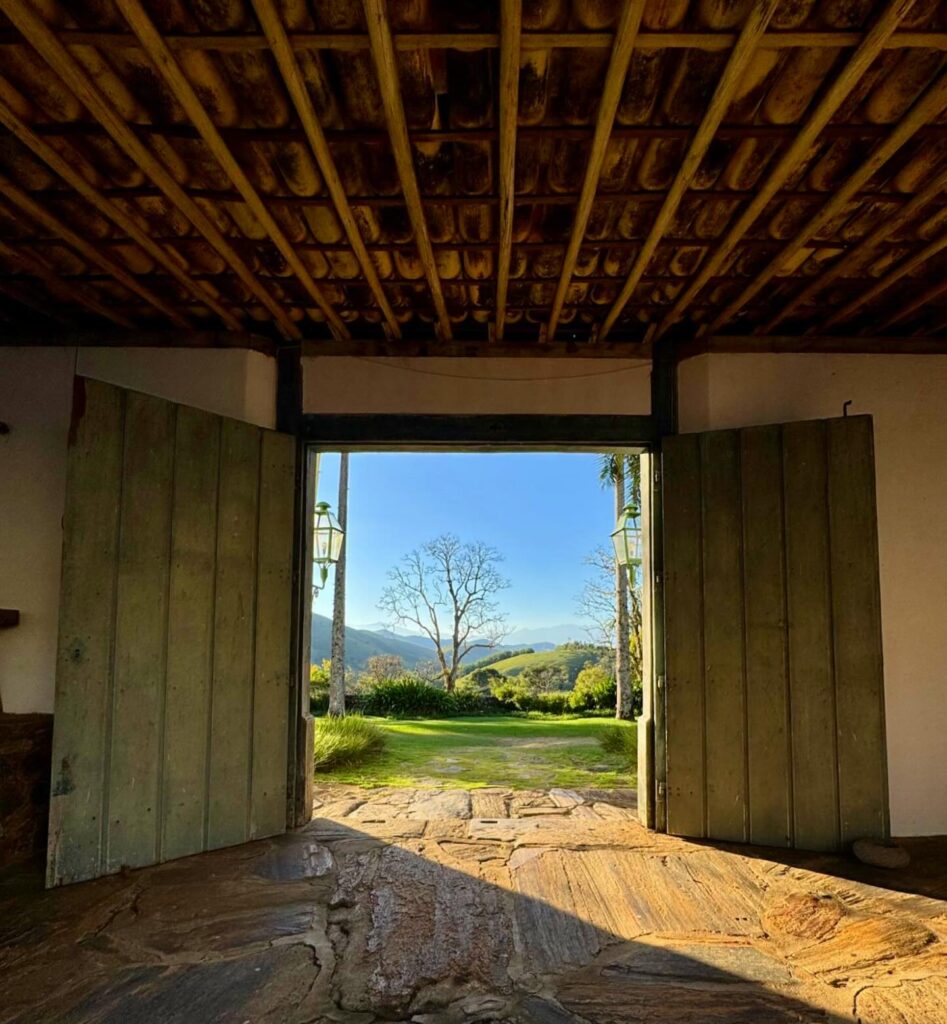Vista de paisagem montanhosa através de grandes portas de madeira em arquitetura colonial brasileira de fazenda.