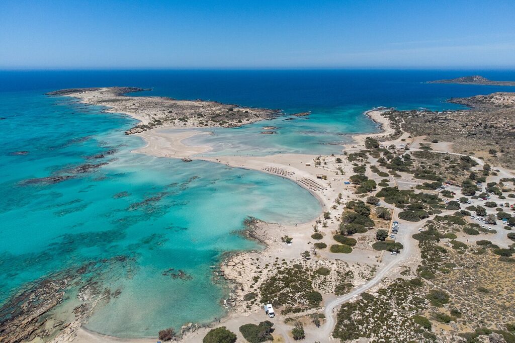 Vista aérea da Praia de Elafonisi na Ilha de Creta, destacando o mar azul turquesa e os bancos de areia branca e rosa.