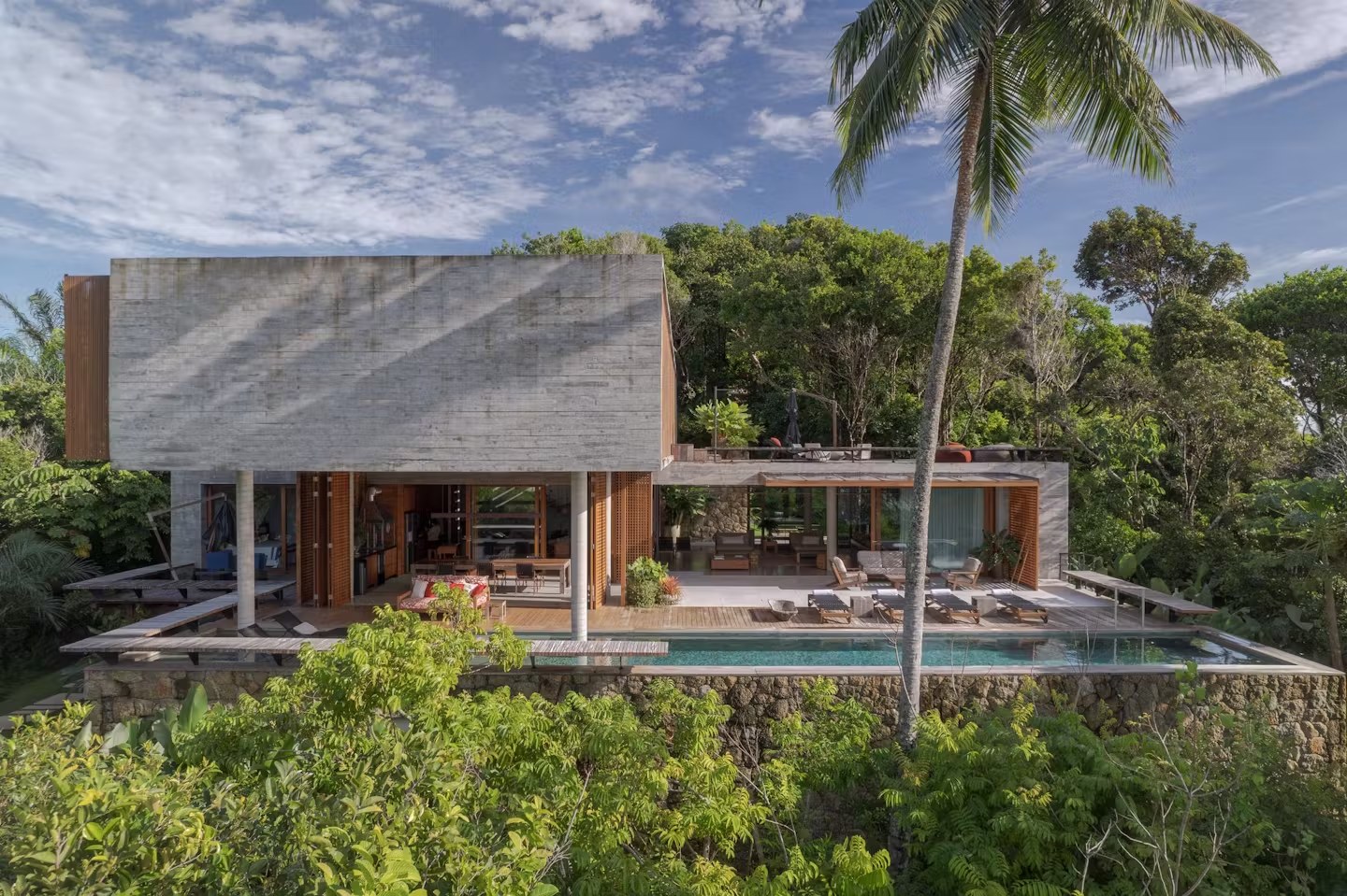 Fachada de casa de luxo para alugar em Itacaré com piscina de borda infinita, concreto aparente e arquitetura integrada à natureza tropical.