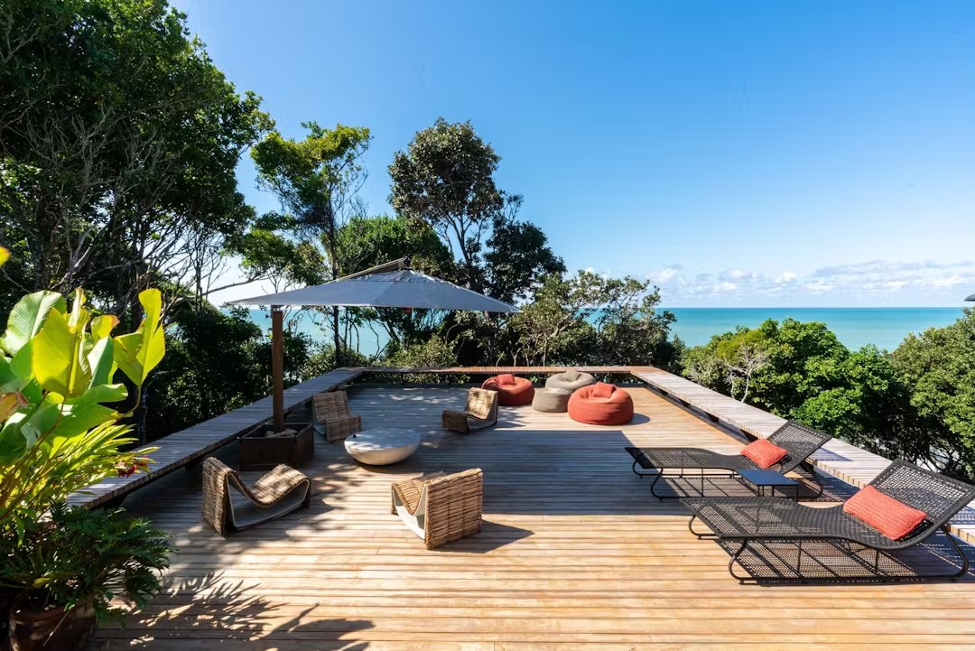 Terraço com vista para o mar em casa de luxo para alugar em Itacaré, apresentando deck de madeira e mobiliário de lazer sofisticado.