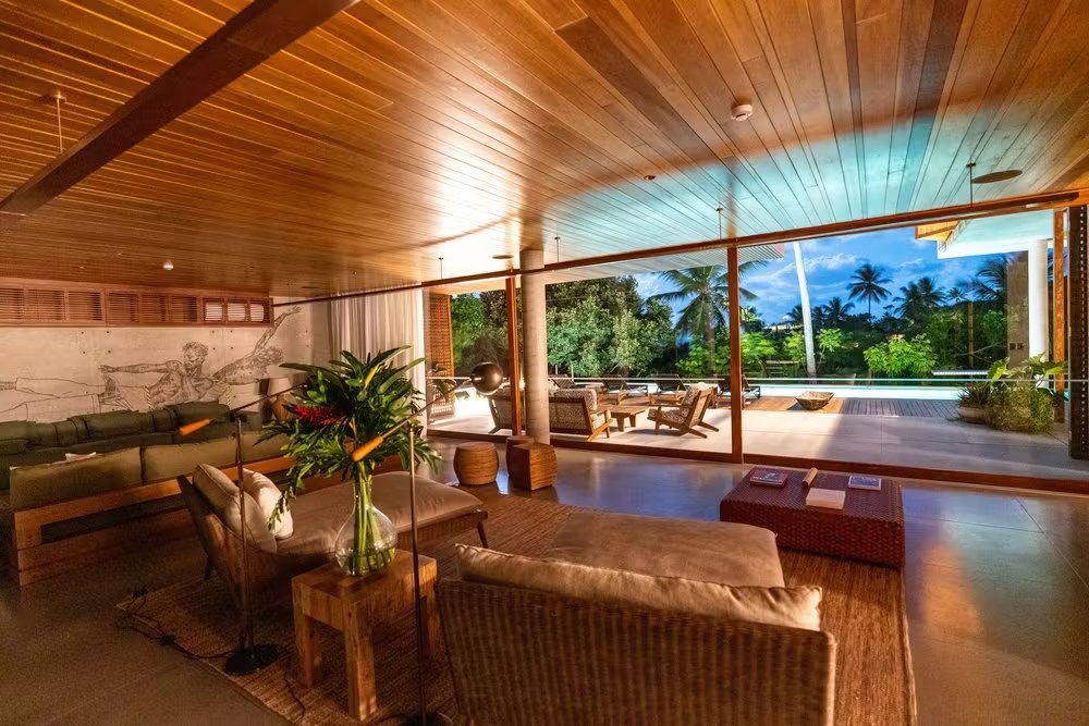 Sala de estar integrada ao deck em casa de luxo para alugar em Itacaré, destacando o uso de materiais naturais e arquitetura aberta.