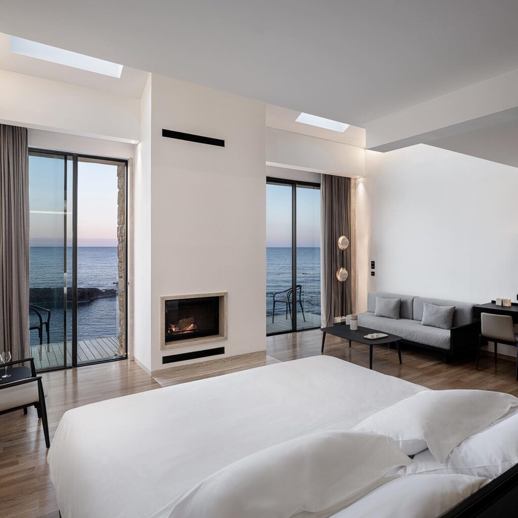 Suíte moderna com lareira e varanda frente mar, exemplificando o design dos melhores hoteis da ilha de creta.