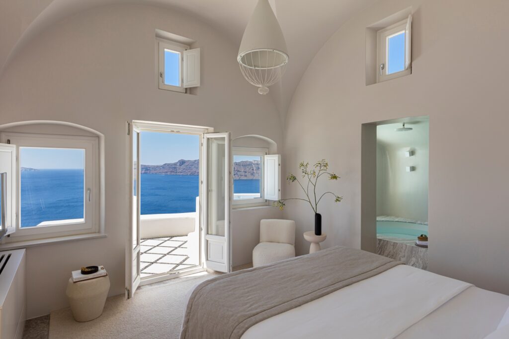 Suíte luxuosa em hoteis boutique em santorini com vista para o mar e design minimalista em tons de branco.