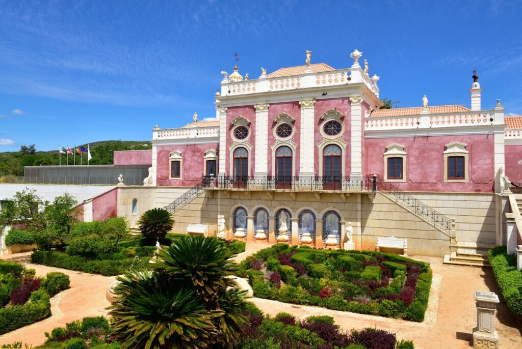 Fachada de palácio rosa com jardins franceses, exemplo de arquitetura luxuosa em pousadas em portugal.