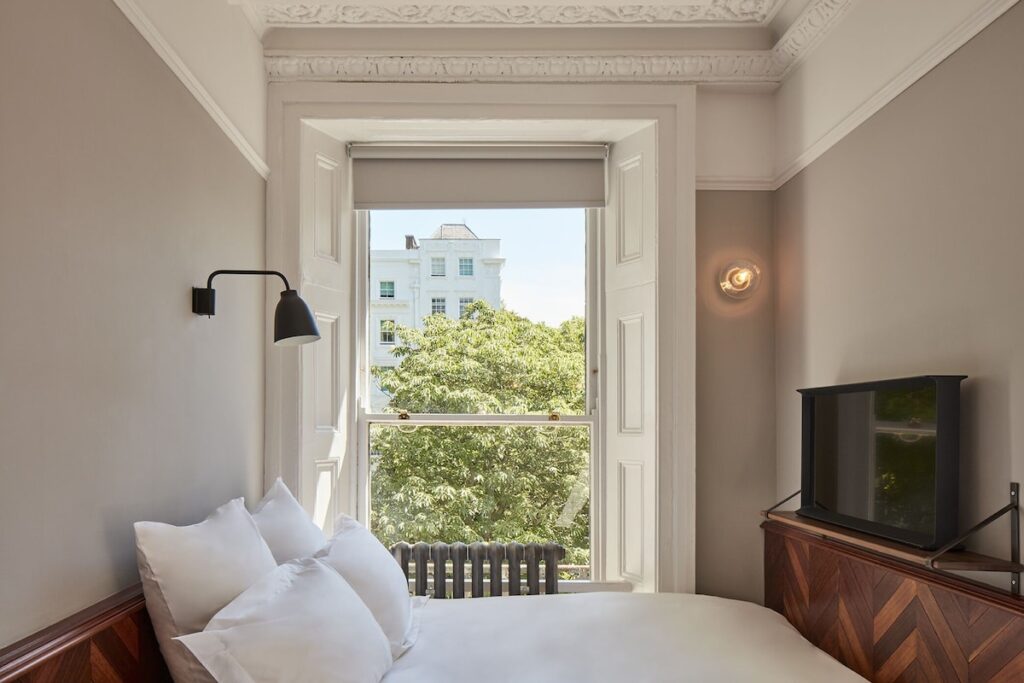 Quarto minimalista com teto vitoriano ornamentado e cabeceira de madeira em hotéis boutique em londres.
