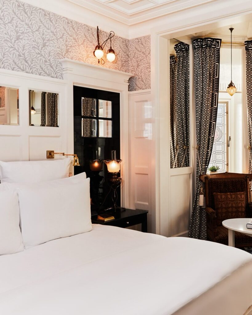 Quarto de luxo em hotéis boutique em londres com papel de parede floral, móveis brancos clássicos e luminárias Art Nouveau.