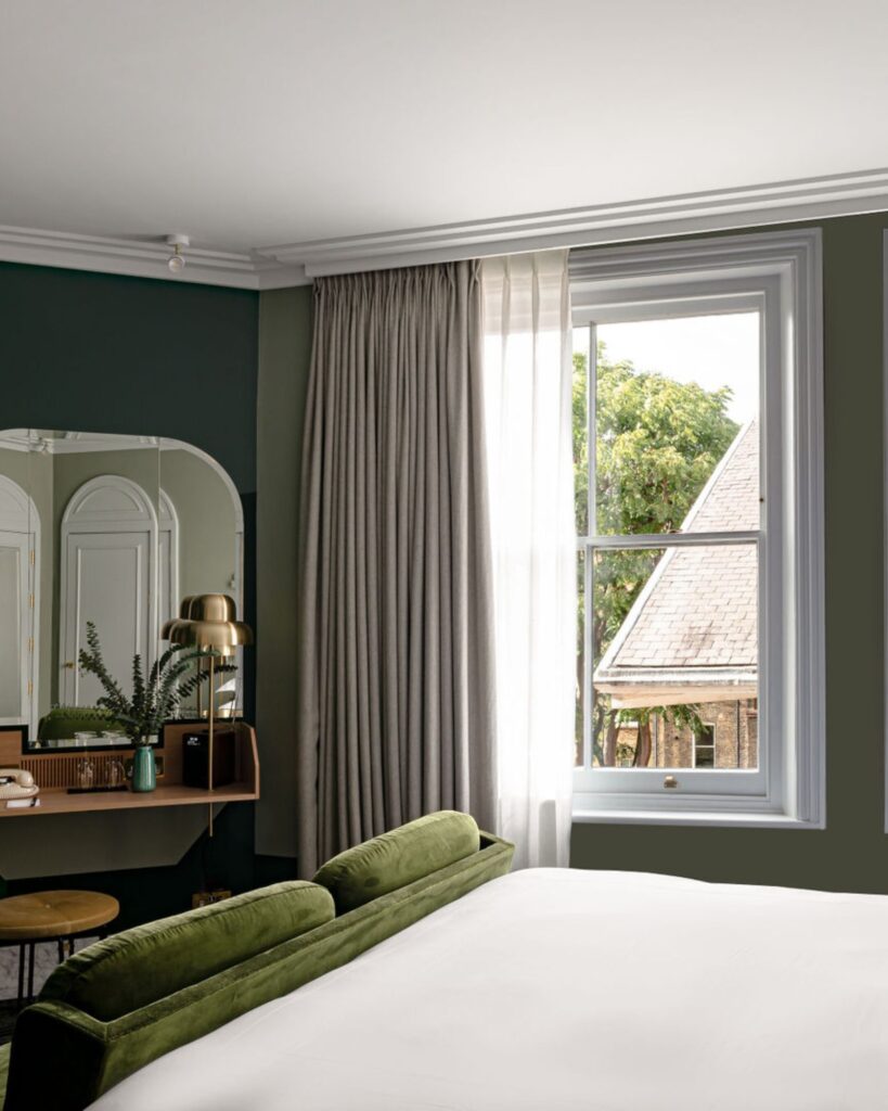 Quarto de design em hotéis boutique em londres com paredes verdes, móveis de madeira e detalhes em latão.