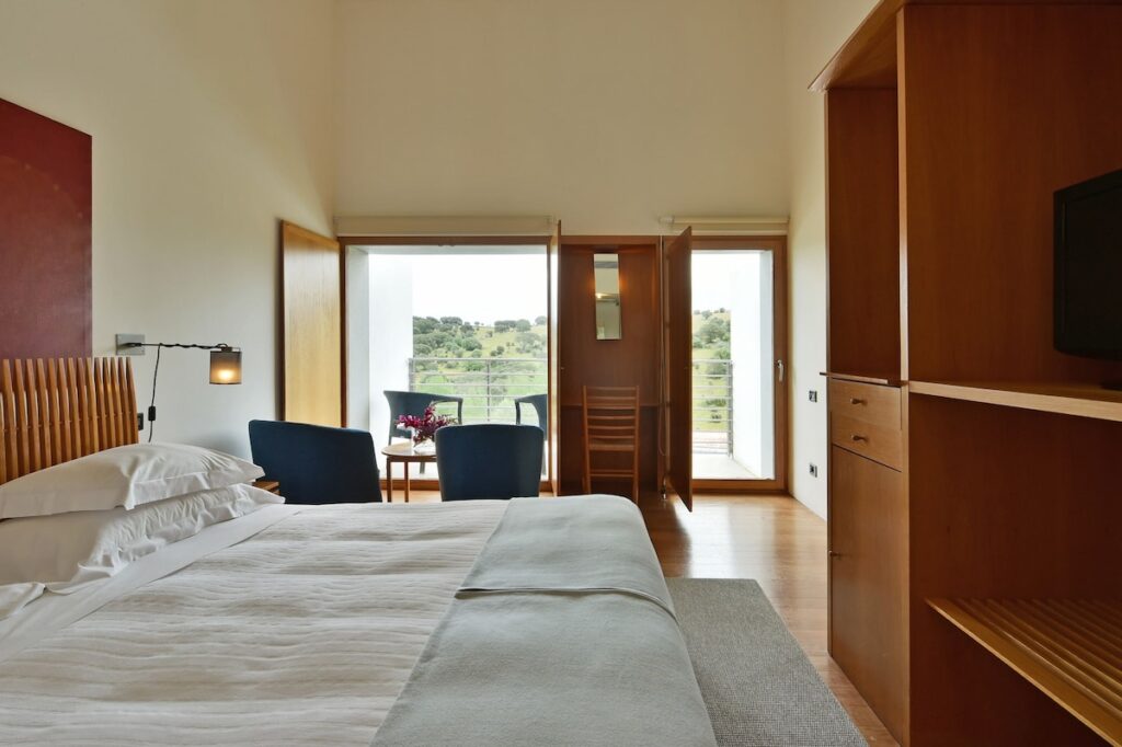 Quarto minimalista com móveis de madeira e vista para o campo, estilo das pousadas em portugal contemporâneas.