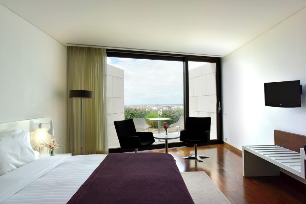 Quarto moderno com ampla janela e design minimalista, contraste arquitetônico nas pousadas em portugal.