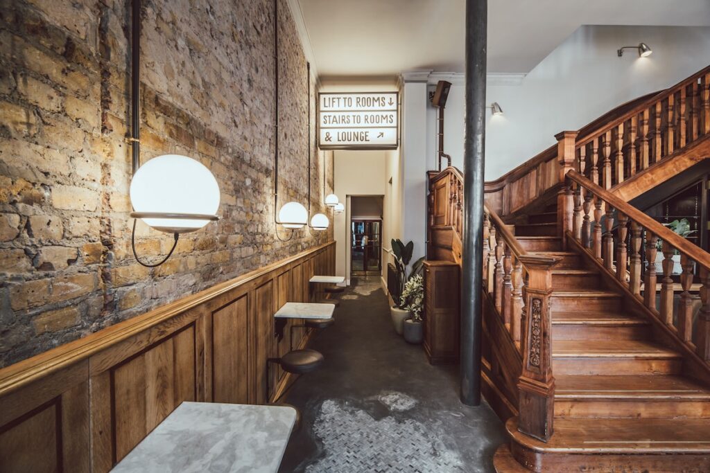 Corredor industrial com tijolos aparentes e escadaria de madeira restaurada em hotéis boutique em londres.
