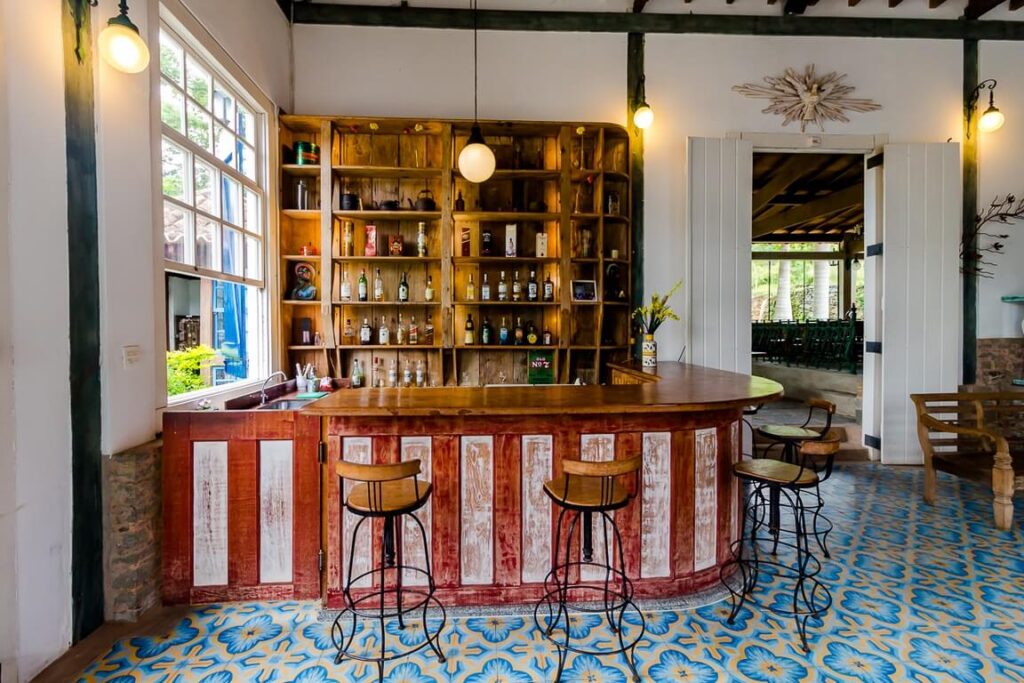 Bar rústico com piso de ladrilho hidráulico e balcão de portas antigas em fazendas históricas para se hospedar.