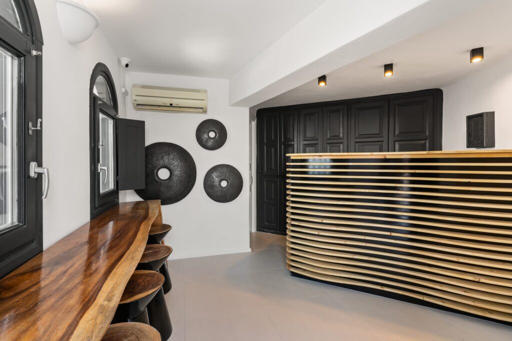 Recepção moderna com balcão de ripas de madeira e design P&B em hoteis boutique em santorini.