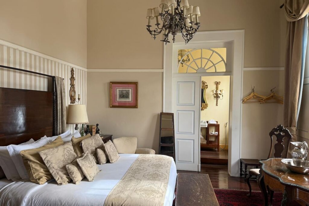 Suíte imponente com cama de madeira maciça e lustre de cristal, destaque entre fazendas históricas para se hospedar.