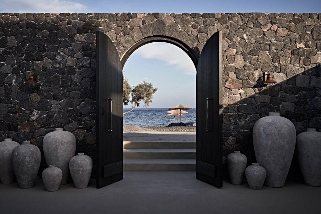 Entrada monumental com arcos de pedra e vasos rústicos em hoteis boutique em santorini.