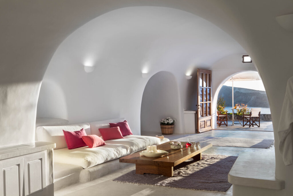 Interiores esculpidos com sofás em alvenaria e toques de cor fúcsia em hoteis boutique em santorini.