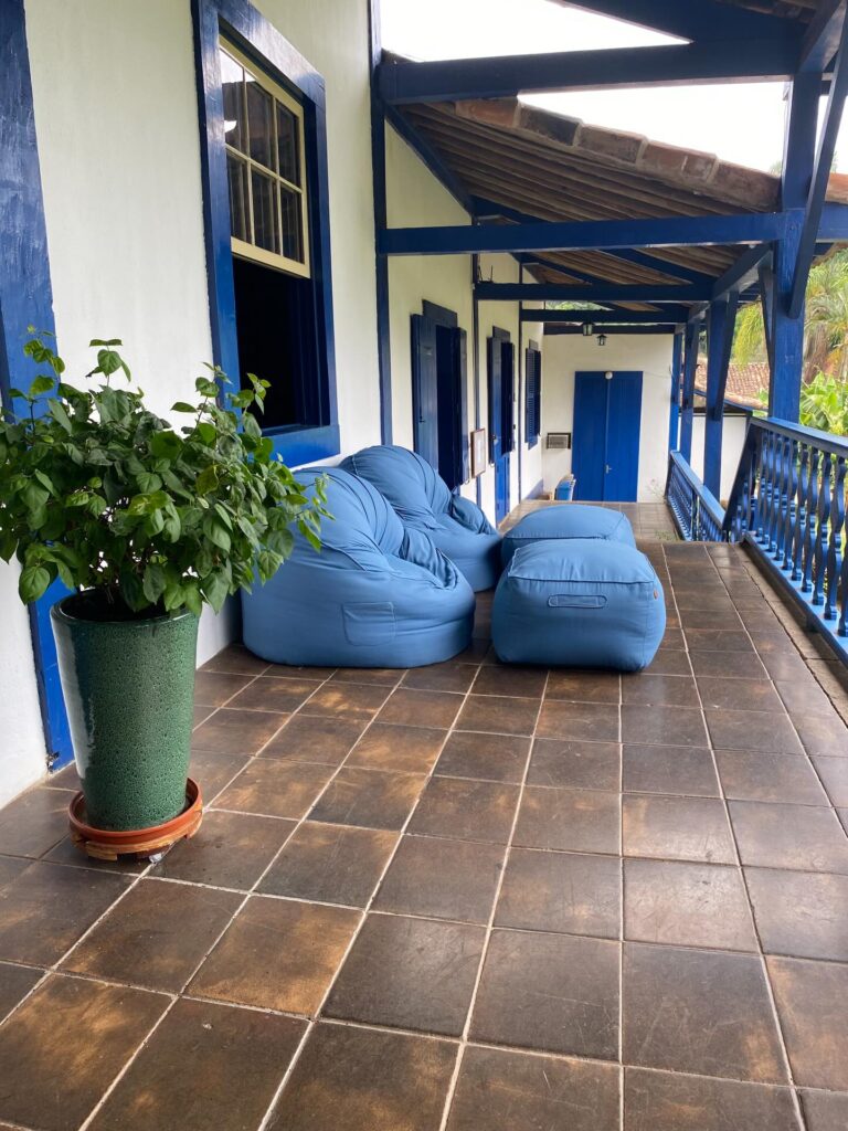 Pufes azuis em varanda de fazenda colonial com arquitetura preservada, exemplo de fazendas históricas para se hospedar.