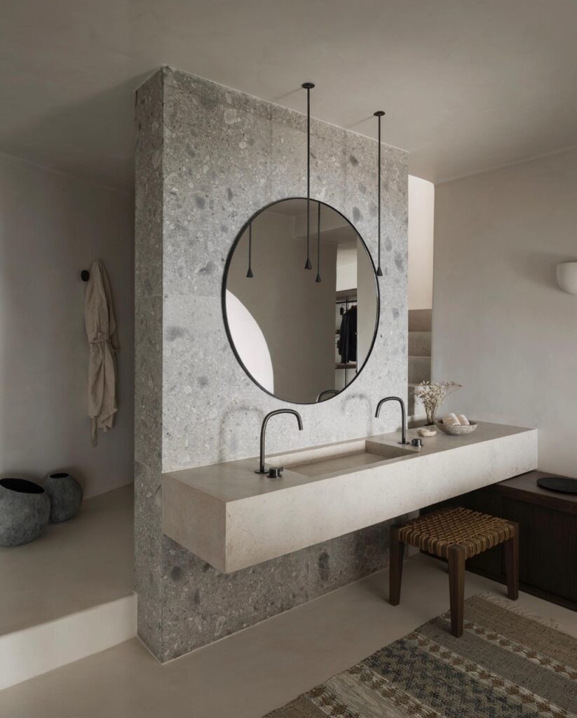 Banheiro de design com bancada de pedra e espelho circular em hotéis boutique em santorini de alto padrão.