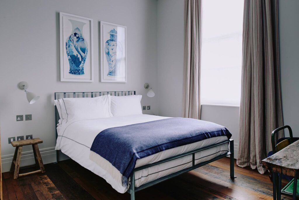 Quarto minimalista de hotéis boutique em londres com cama de ferro, piso de madeira de demolição e quadros azuis.