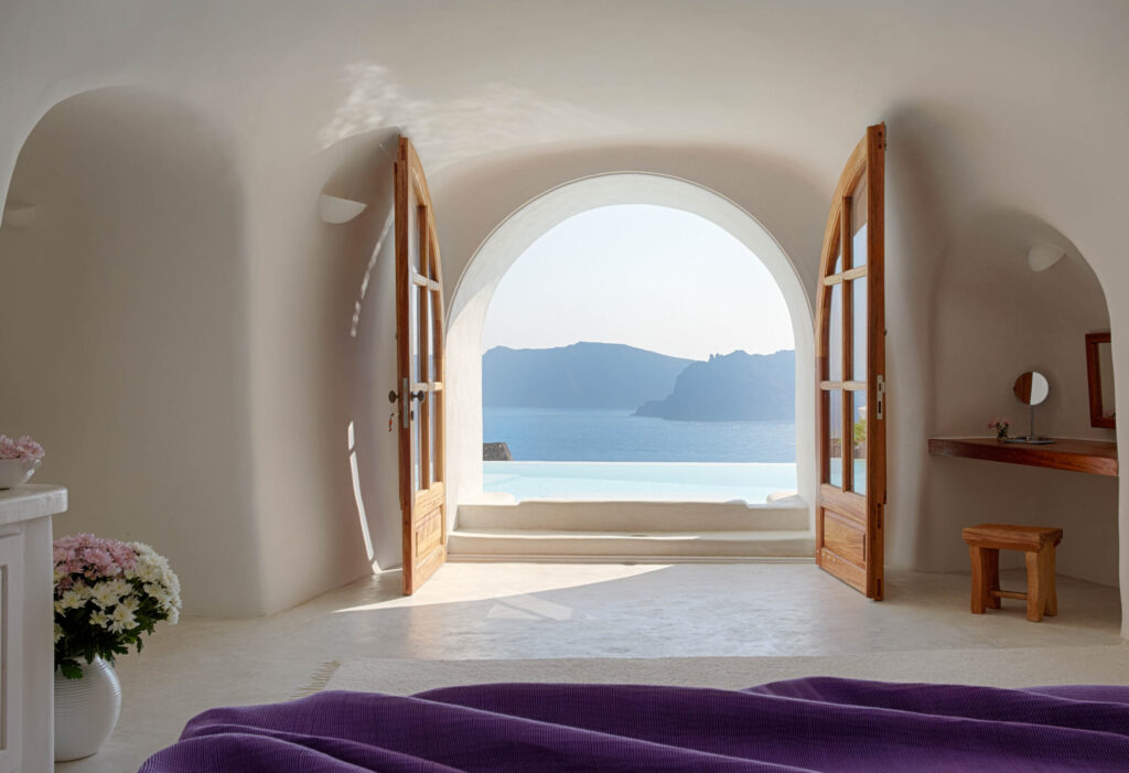 Quarto com vista deslumbrante através de portas em arco em hoteis boutique em santorini.
