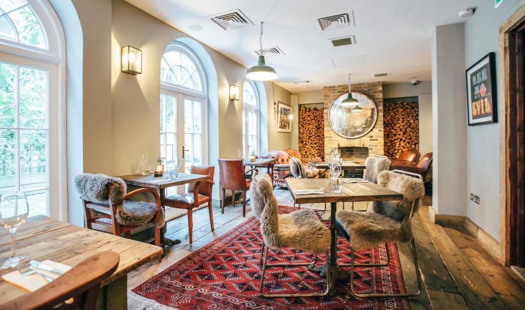 Restaurante de hotéis boutique em londres com mesas de madeira rústica, cadeiras de pele e tapete persa.