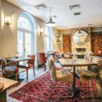 Restaurante de hot&eacute;is boutique em londres com mesas de madeira r&uacute;stica, cadeiras de pele e tapete persa.