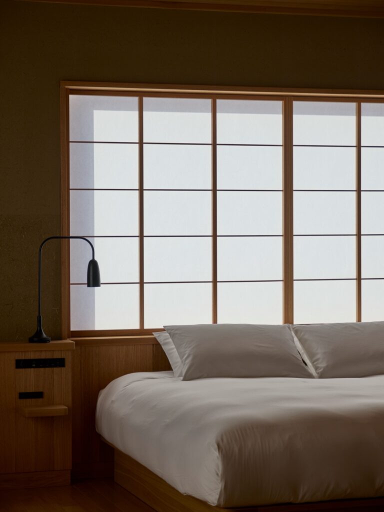 Detalhe de quarto minimalista com cama branca e telas shoji no Azuma Farm Koiwai.